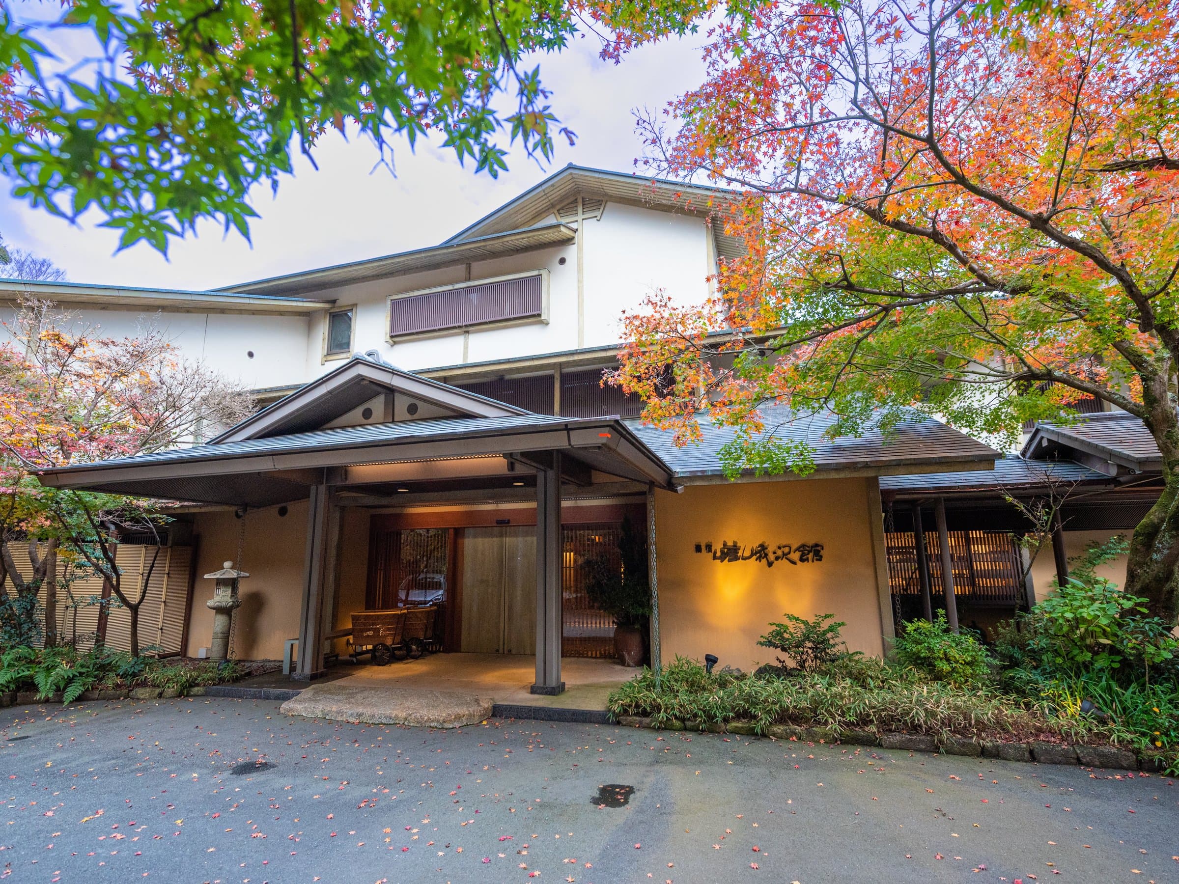 Wooden entrance and main building of Yuyado Sagasawakan ryokan framed by autumn maple foliage in Yugashima, Izu