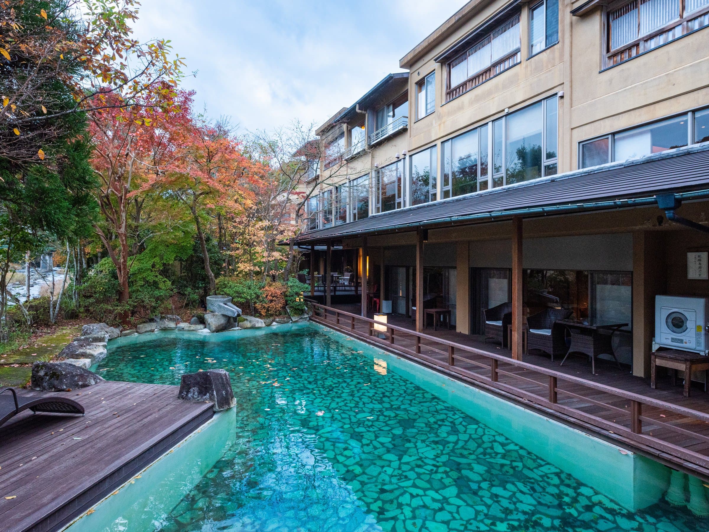Outdoor hot-spring pool beside the wooden main building and autumn maples at Sagasawakan in Yugashima, Izu