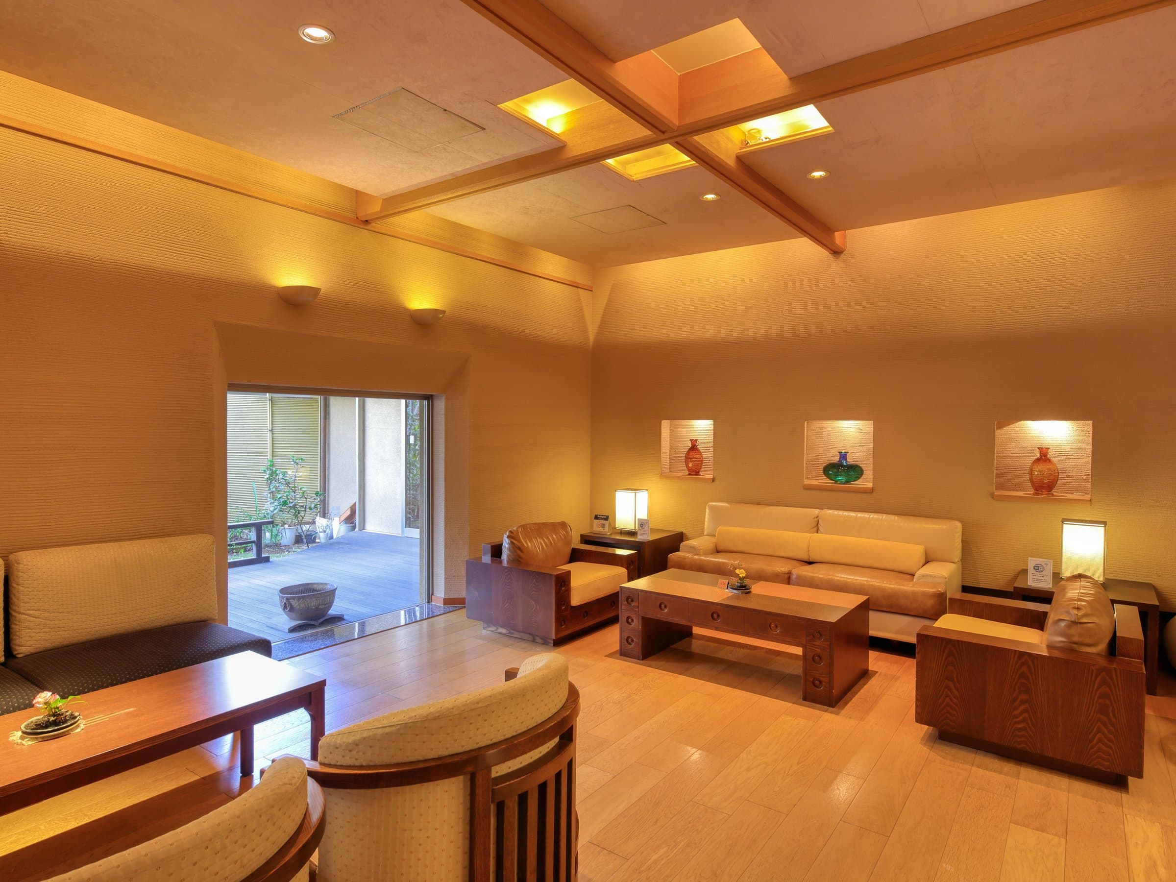 Warmly lit lounge with low sofas, coffee tables and a courtyard garden view at Sagasawakan ryokan