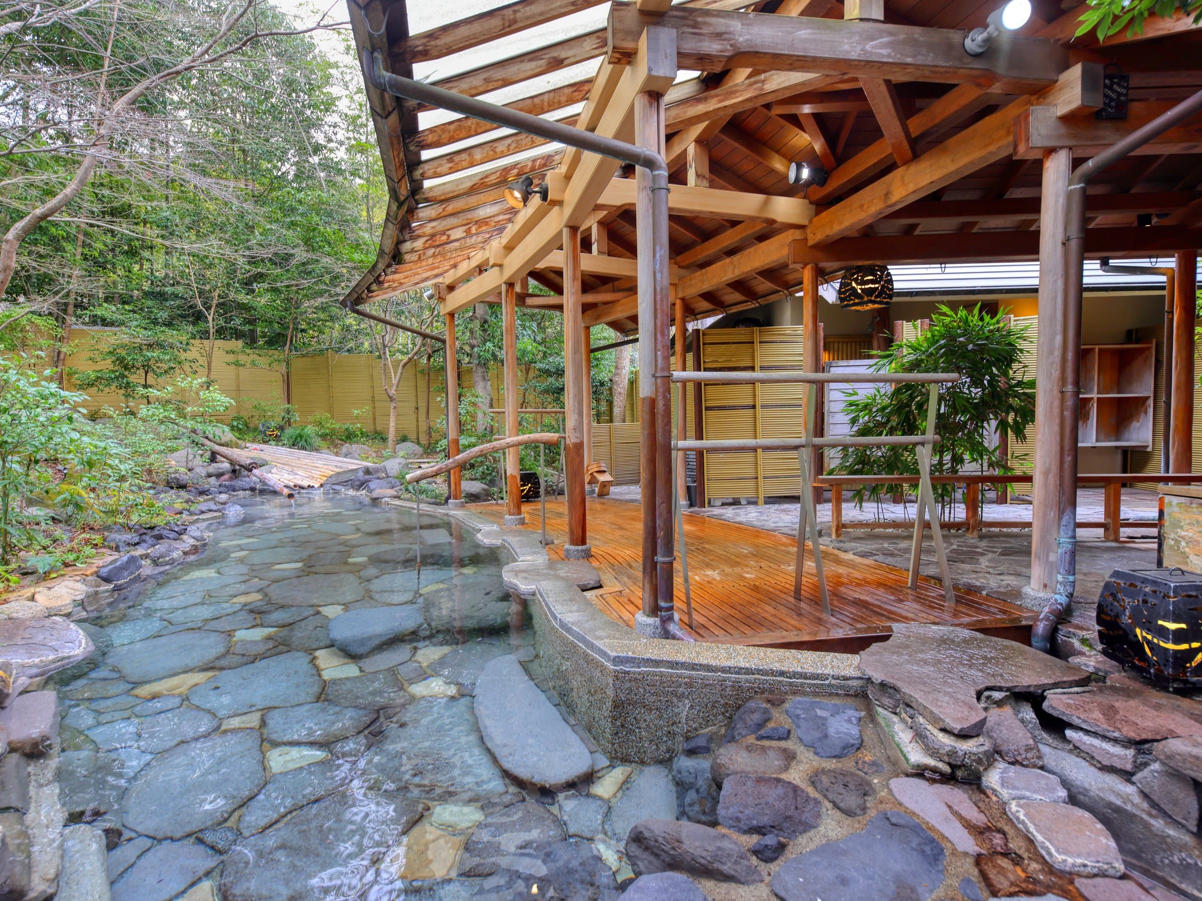 Open-air stone rotenburo hot-spring bath under a timber pavilion surrounded by greenery at Sagasawakan, Izu