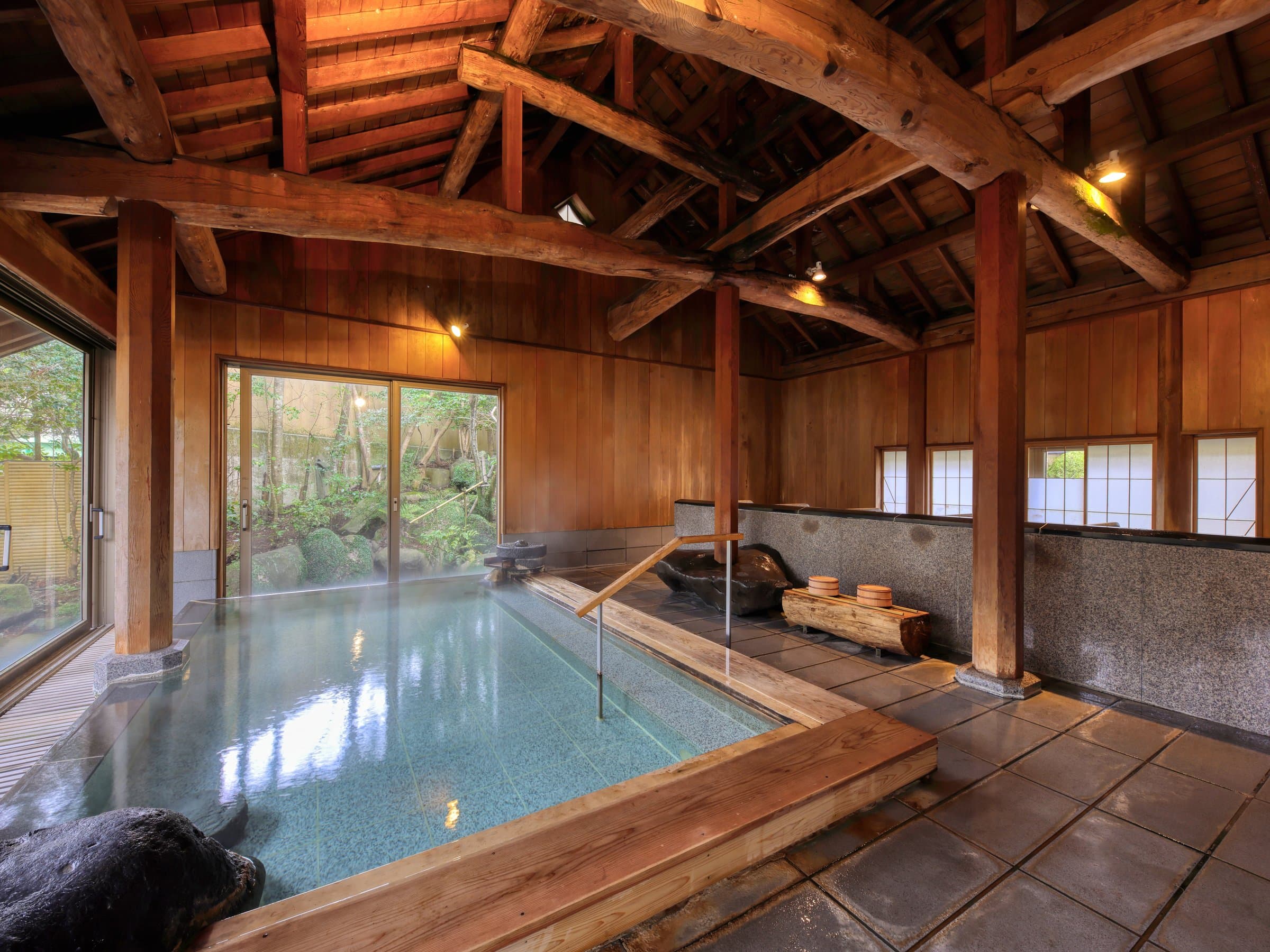 Indoor wooden onsen bath with exposed timber beams and a garden view at Sagasawakan in Yugashima, Izu