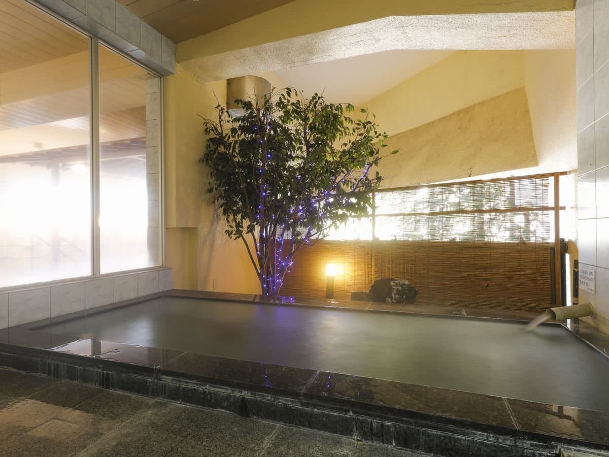 Indoor onsen bath with an illuminated tree and bamboo screen at Hotel Katsuragi, Dogo Onsen