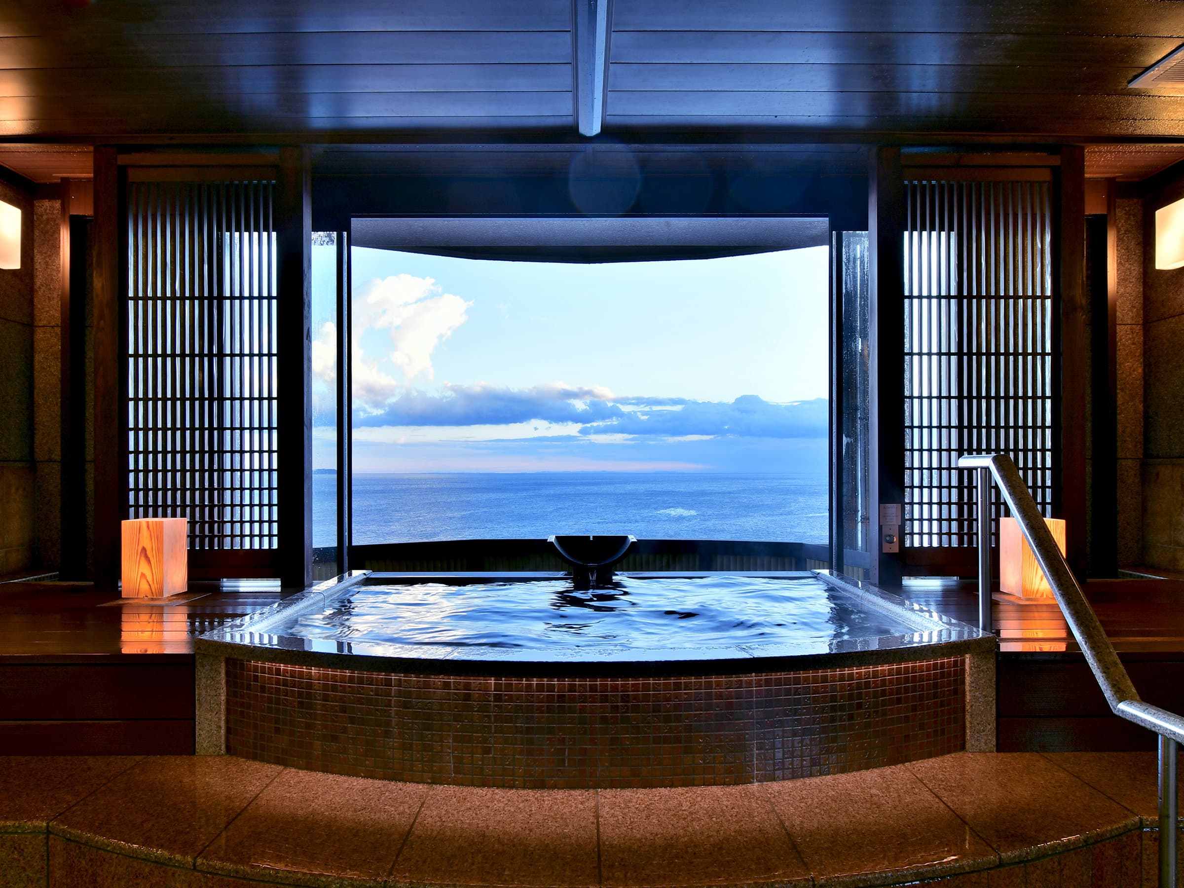 Indoor hot spring bath framed by shoji screens with a wide panoramic ocean view in Izu
