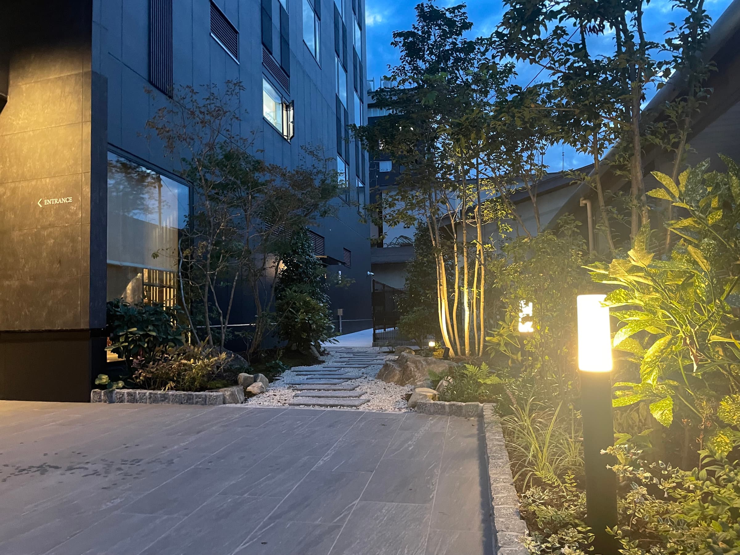 Lantern-lit garden entrance path with stone steps and greenery at dusk