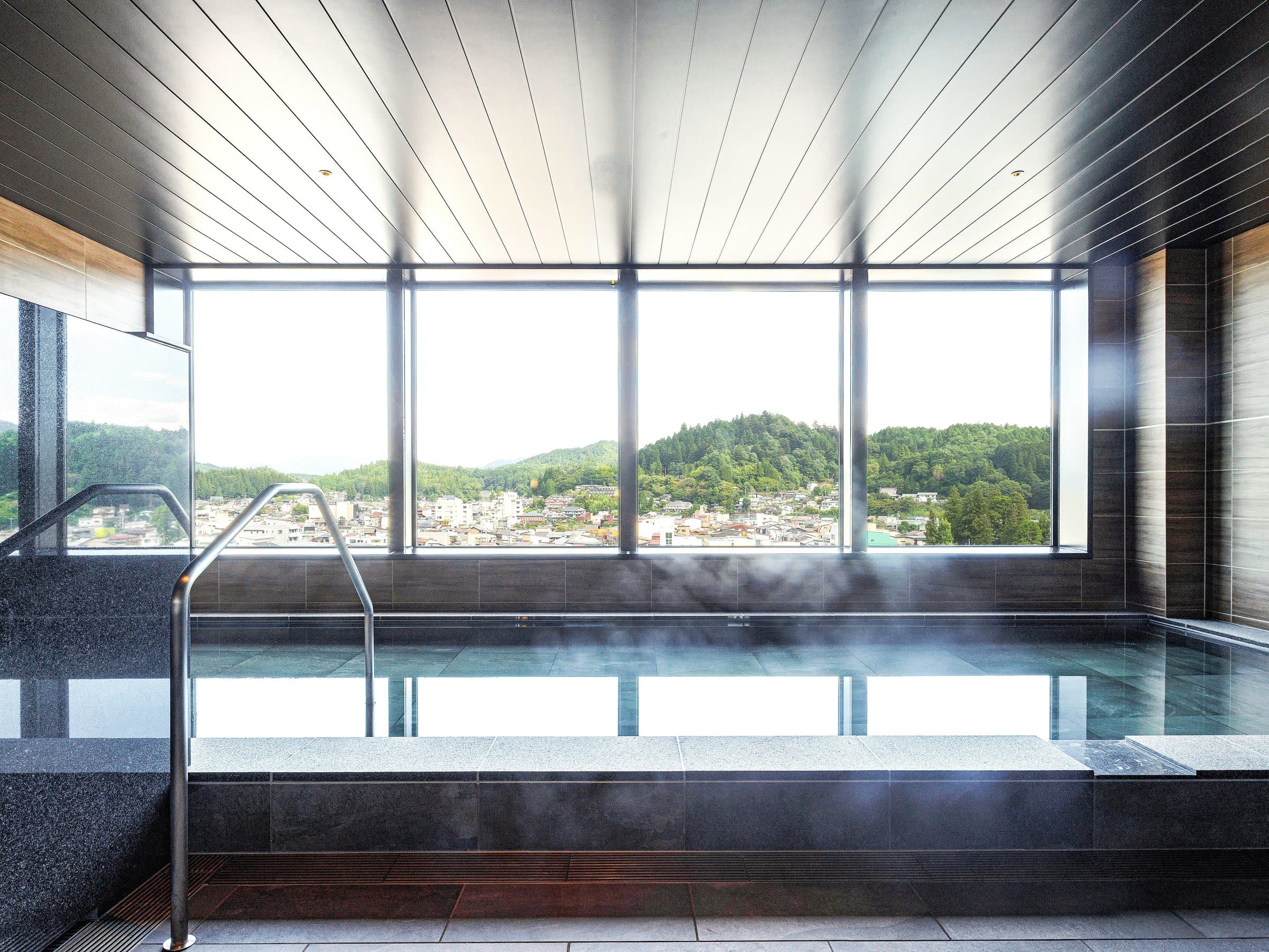 Indoor hot spring bath with steam and panoramic window view of Takayama's hills