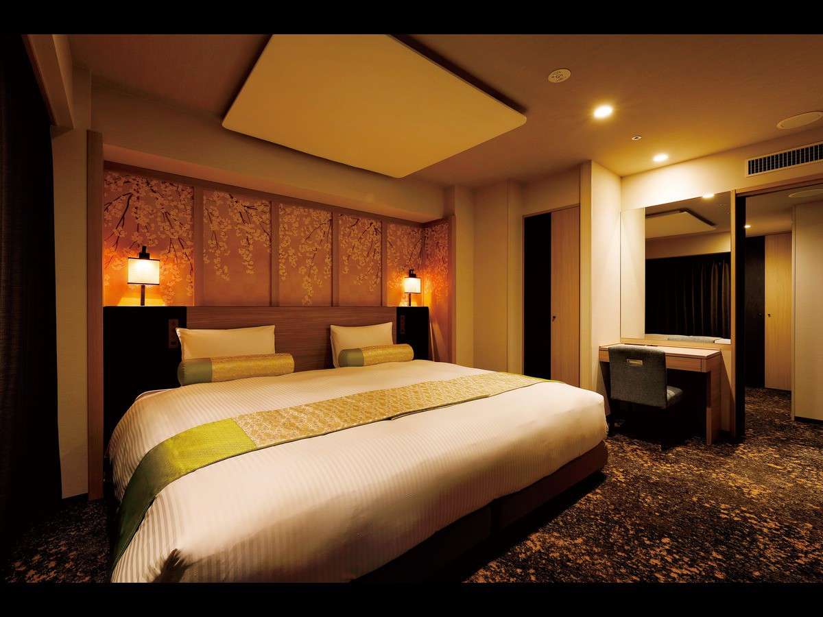 Warmly lit premium guest room with a wide bed, cherry-blossom mural headboard and dressing desk at Daiwa Roynet Hotel Nara