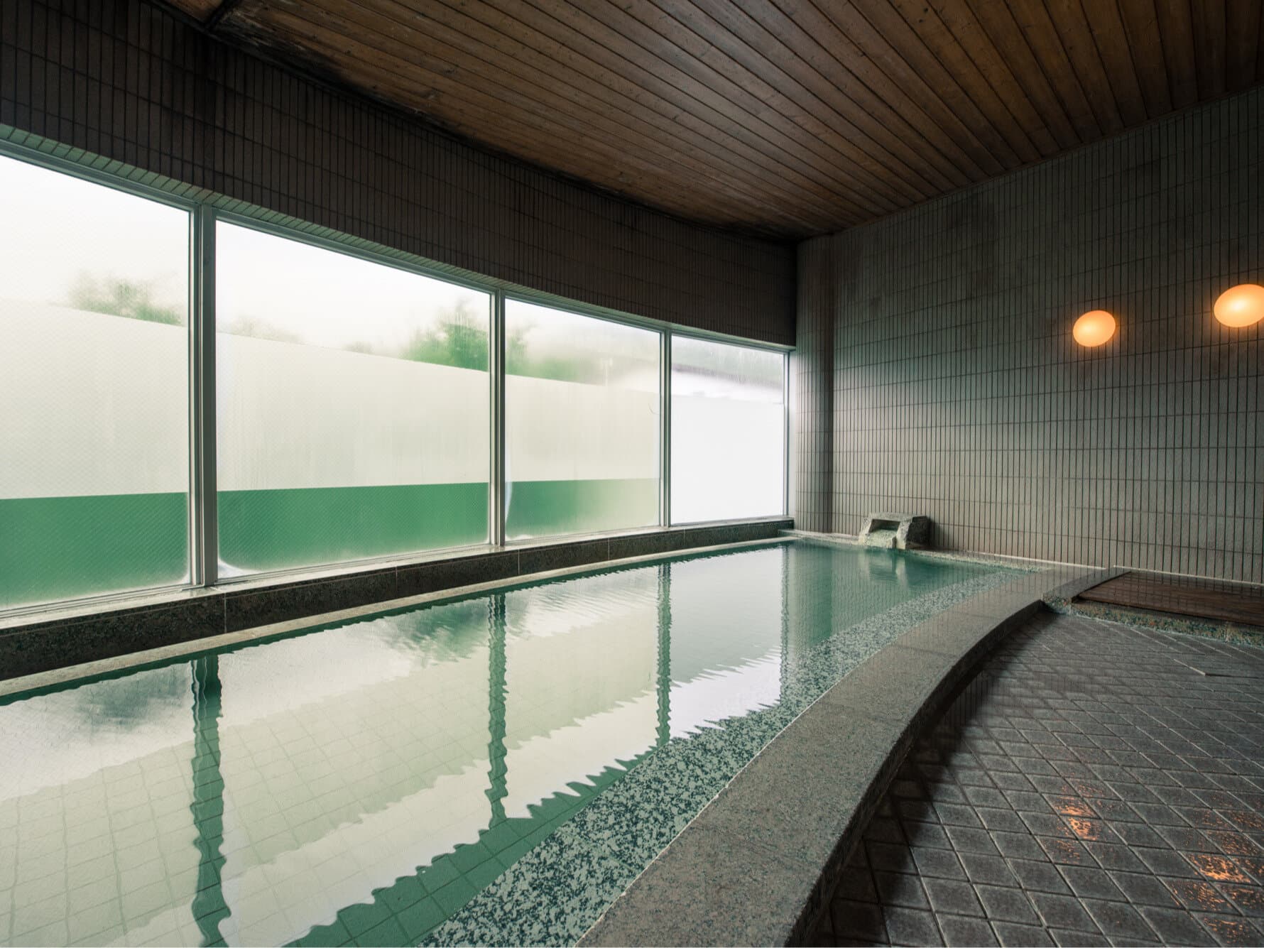 Spacious indoor public bath at Takamiya Rurikura Resort with green-tiled pool and wide frosted windows