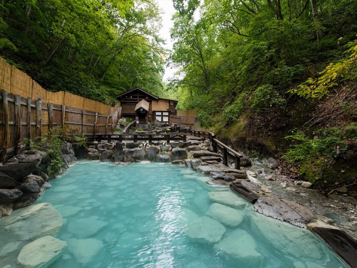 Outdoor rotenburo with milky blue-green Zao sulphur hot spring water surrounded by forest