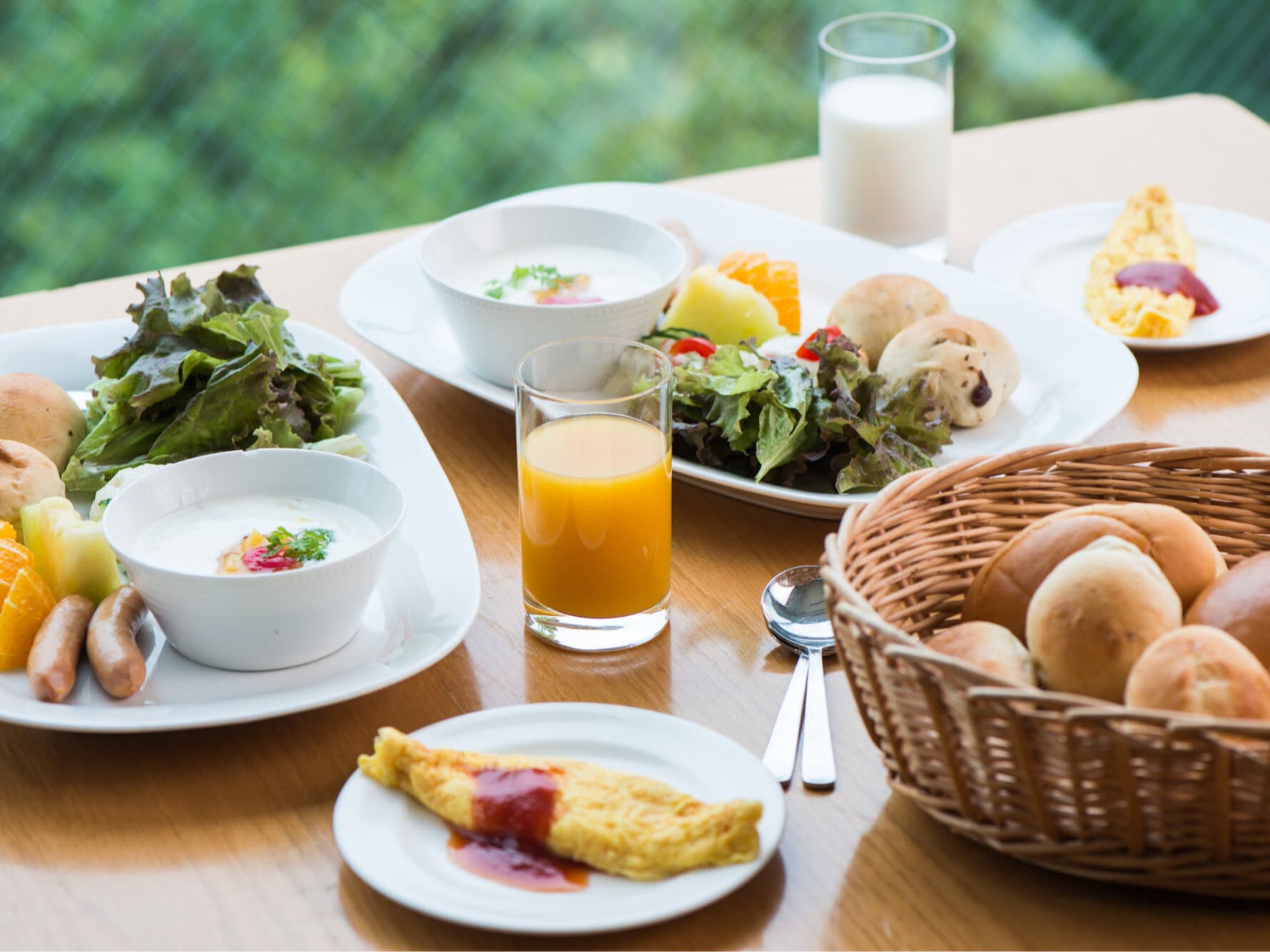 Breakfast set with fresh salad, bread basket, omelette and orange juice by a green view