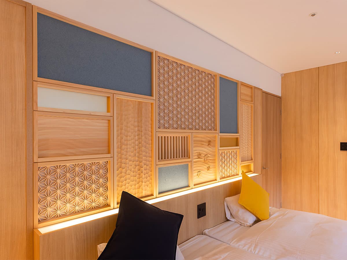 Wa-modern room detail with warm wood and backlit kumiko lattice panels behind the bed headboard