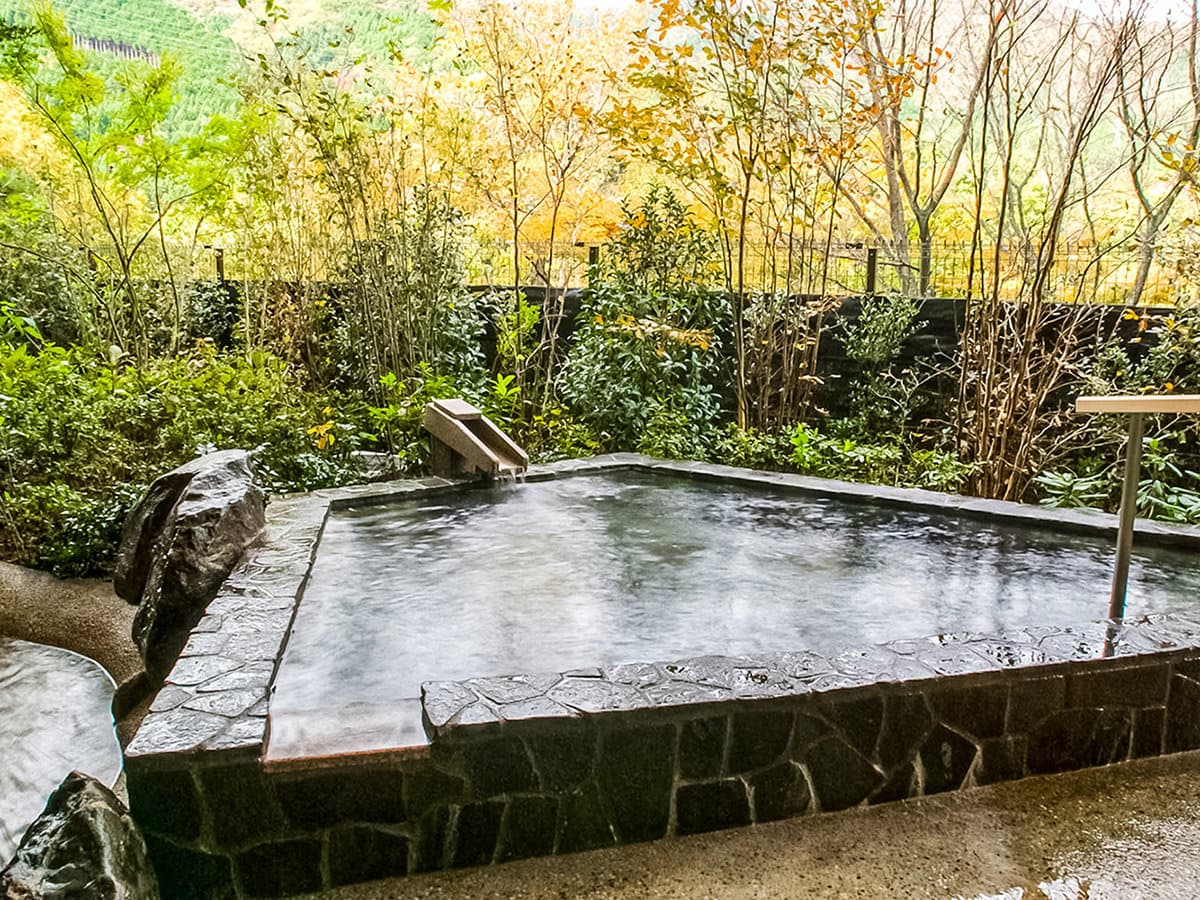 Stone outdoor rotenburo hot-spring bath framed by autumn foliage at Nikko Kinugawa Hotel Mikazuki