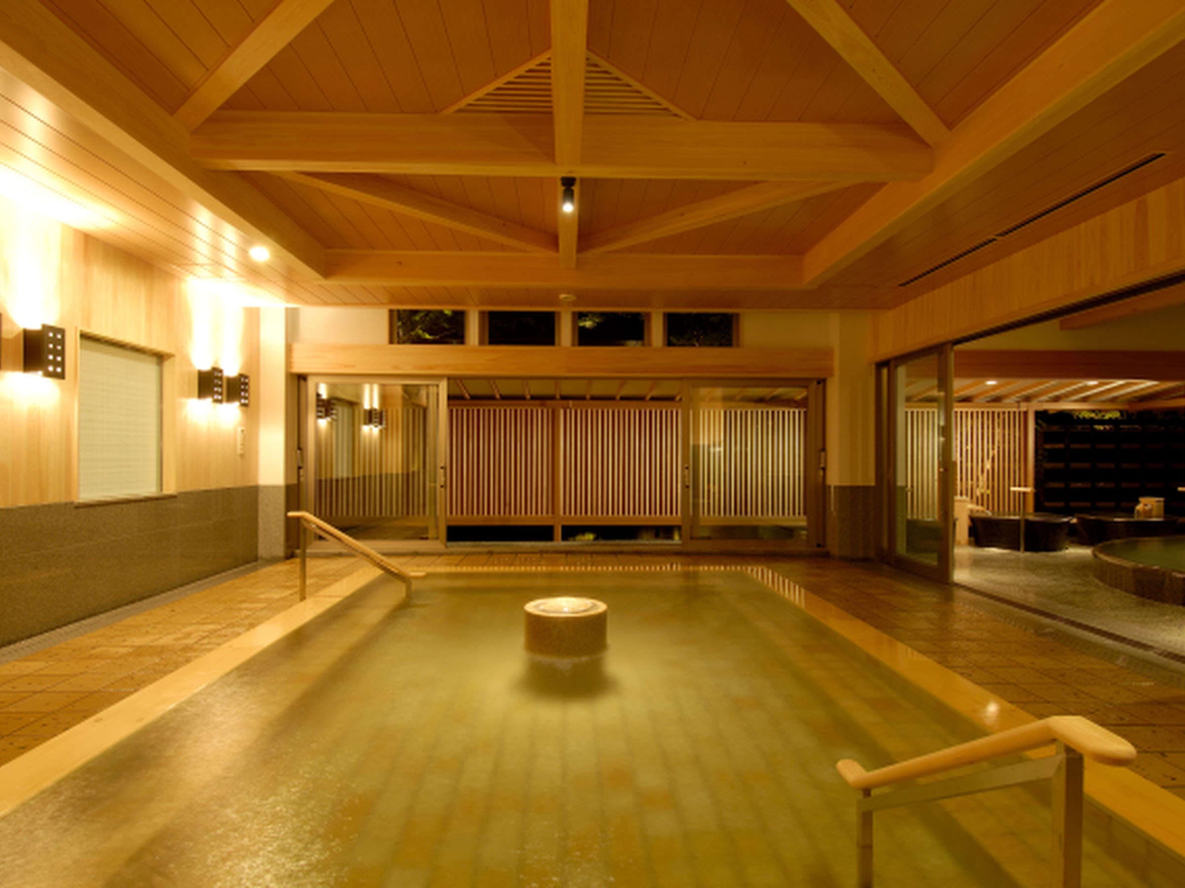 Spacious indoor hot-spring bath with a high timber-beamed ceiling and stone-tiled floor at Hotel New Mitoya, Akiu Onsen