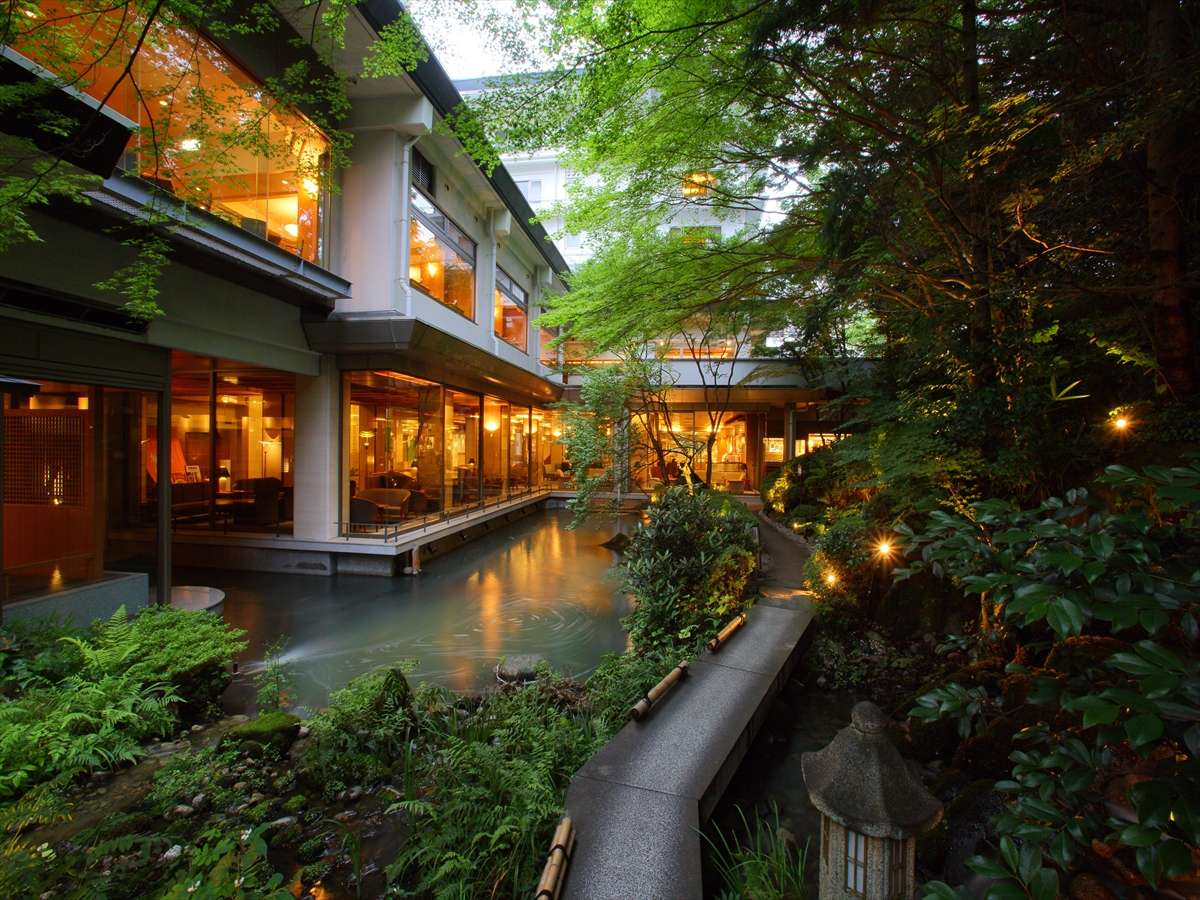 Japanese garden with a stone-lined pond and lit lounge wing of Hotel New Mitoya in Akiu Onsen at twilight