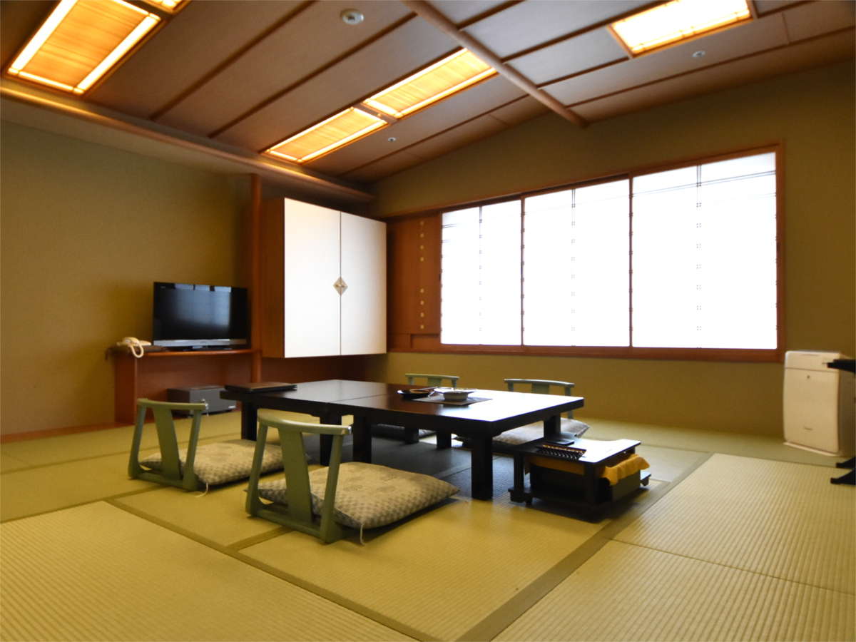 Spacious tatami guest room with low table and floor chairs beneath warm lantern-style ceiling lights at Hotel New Mitoya, Akiu Onsen
