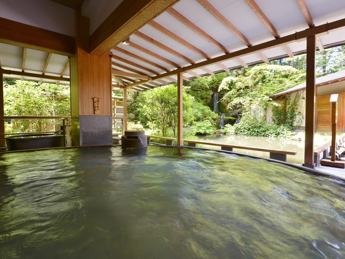 Indoor onsen bath overlooking a garden waterfall and pond through open walls at Hotel New Mitoya, Akiu Onsen