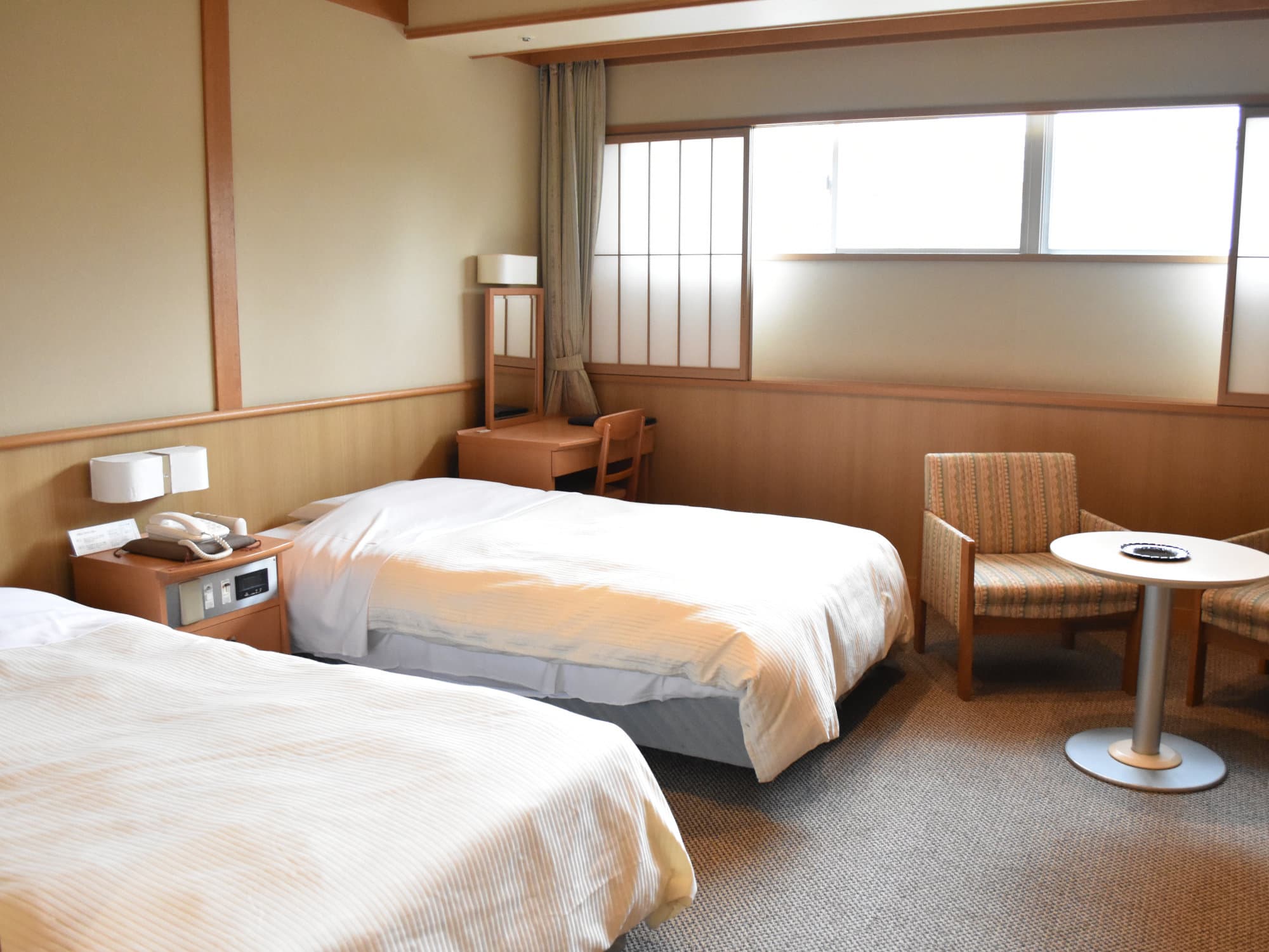 Twin-bed Japanese-Western guest room with armchairs and a bright window at Hotel New Mitoya, Akiu Onsen