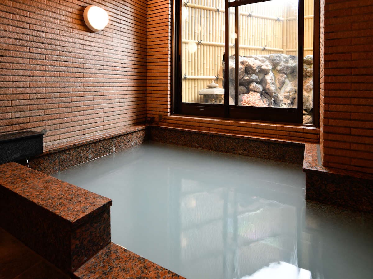 Indoor onsen bath at Ryokan Tamura with milky sulphur spring water and a garden view through the window