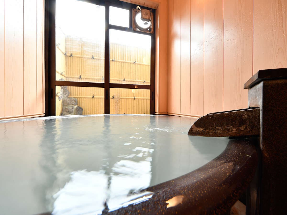 Private reservable kashikiri bath at Ryokan Tamura with a round tub, cypress walls and a bamboo fence outside