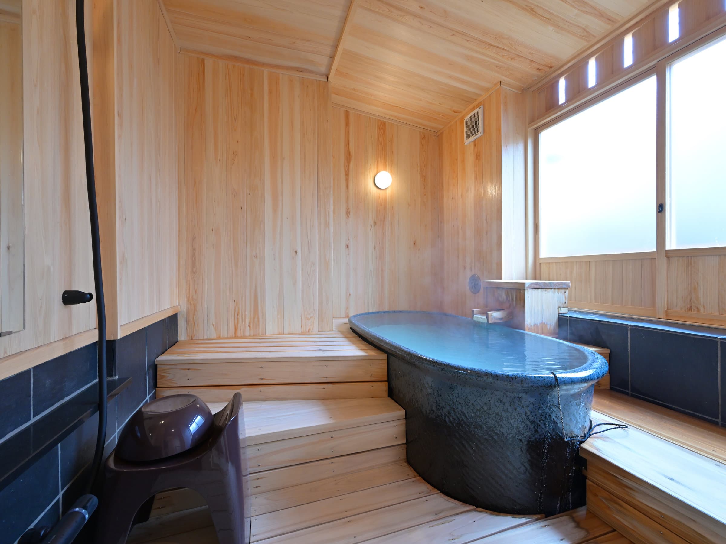 Private in-room hot-spring bath in the Yuri suite at Ryokan Tamura with a blue oval ceramic tub and cypress-panelled walls