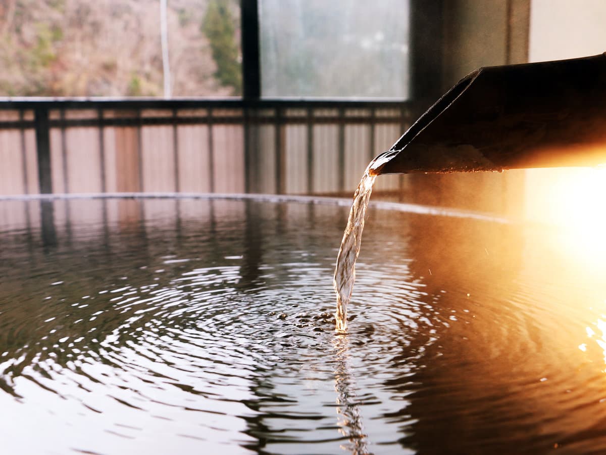 Steaming Ginzan Onsen hot spring water pouring from a bamboo spout into a bath at Showakan