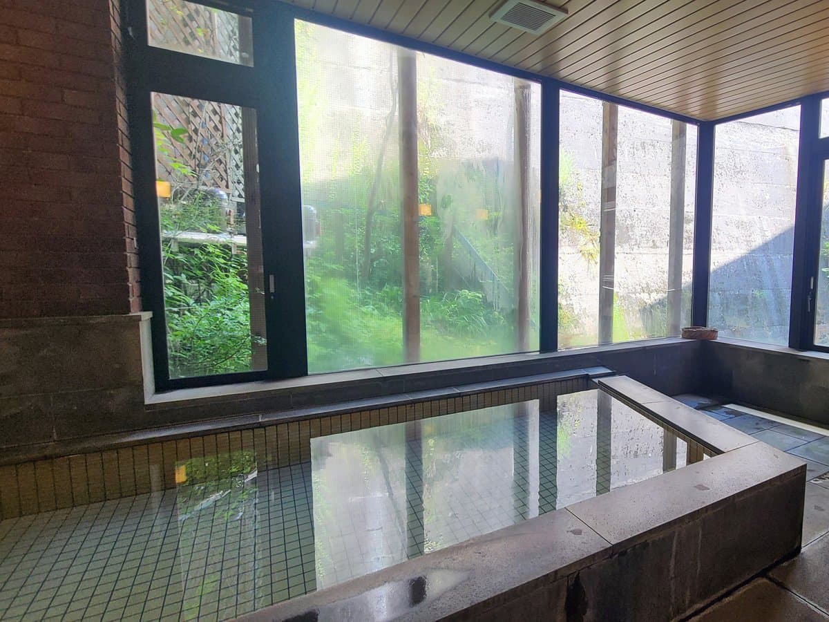 Indoor stone-tiled hot spring bath at Showakan with large windows opening onto a green garden