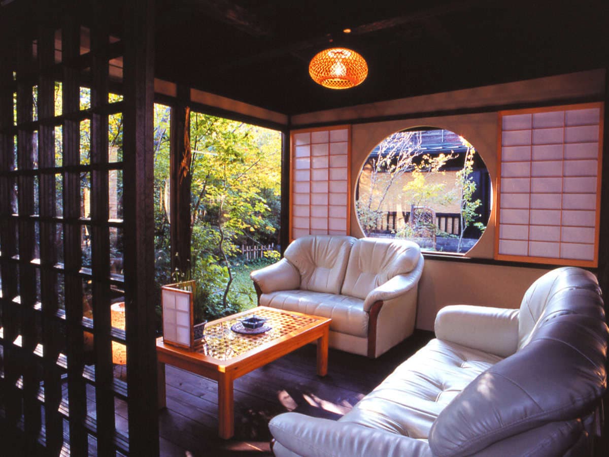 Cozy lounge with leather sofas, round window and warm lantern overlooking a green garden at Onjuku Yagura
