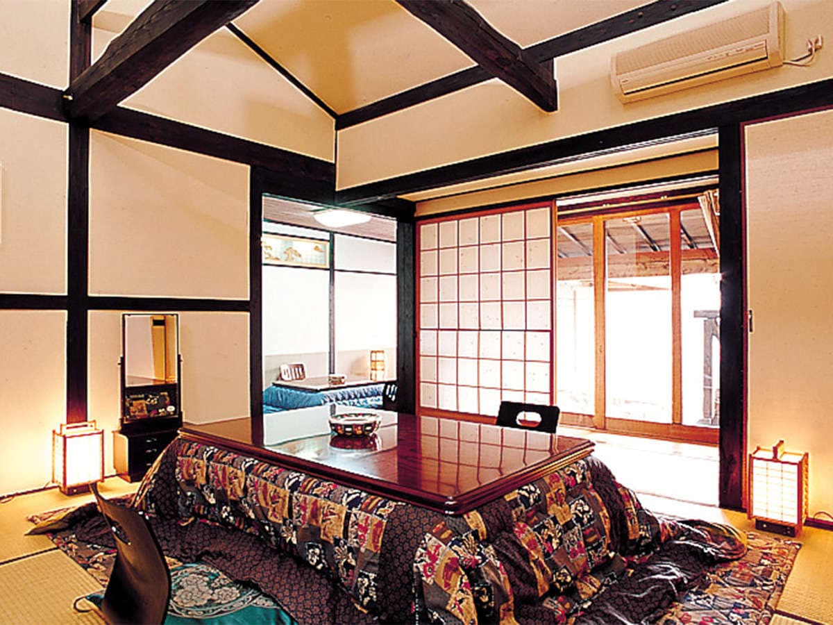 Spacious tatami guest room with exposed dark beams, kotatsu table and shoji screens at Onjuku Yagura