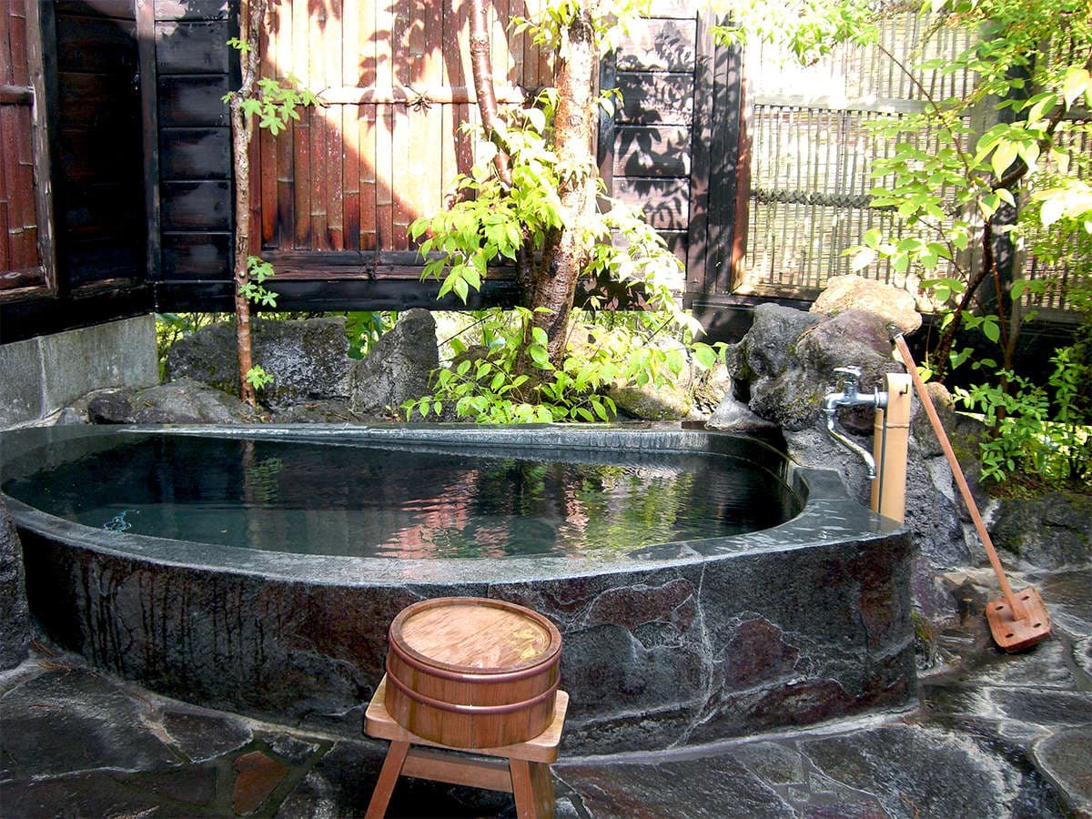 Private outdoor stone rotenburo bath surrounded by greenery and bamboo fencing at Onjuku Yagura, Yufuin