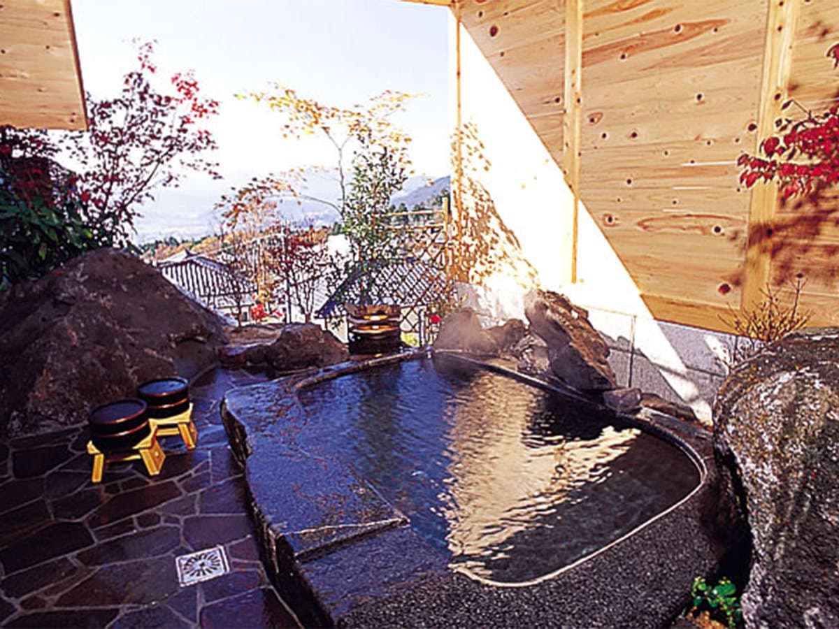 Open-air hot spring bath with distant Yufuin valley and mountain view in evening light at Onjuku Yagura