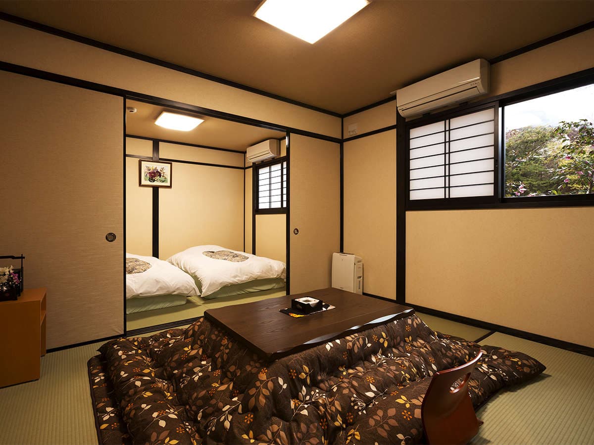 Tatami guest room with futon bedding laid out and a kotatsu, garden view through the window at Onjuku Yagura
