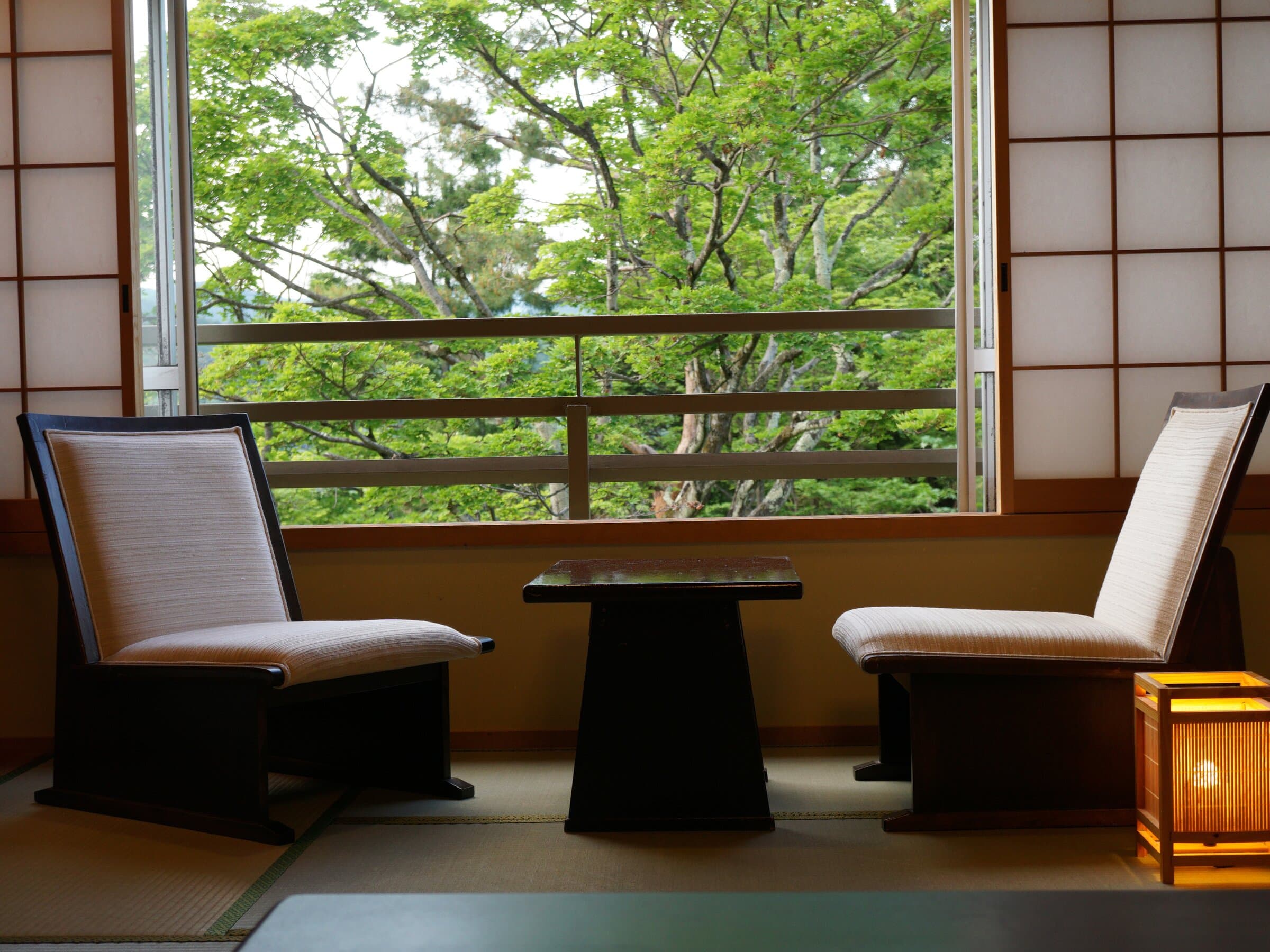 Tatami sitting corner at Nikko Hoshi no Yado with two low chairs, table and lush forest view through the window