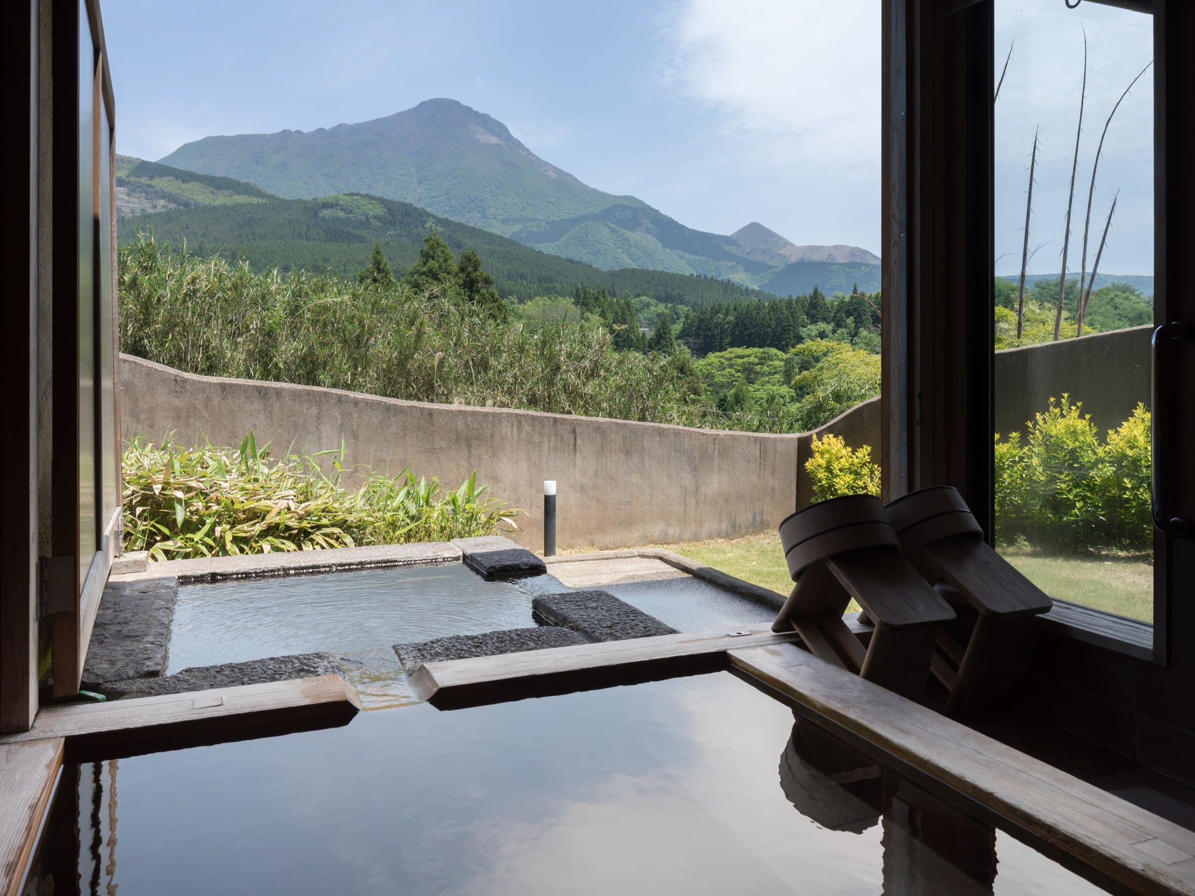 Stone private rotenburo bath beside a window framing Mount Yufu and green Yufuin hills