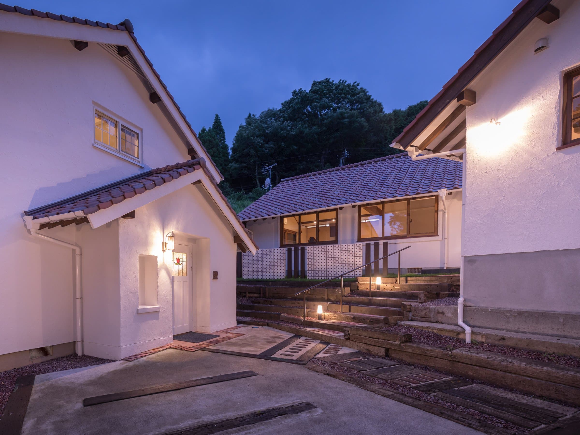 Whitewashed detached guest cottages lit at dusk with tiled roofs and stone steps at Ikkoten in Yufuin