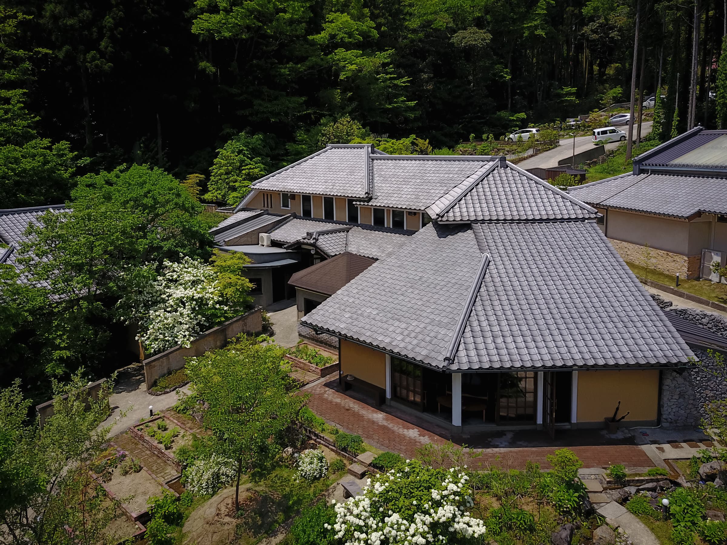 Aerial view of Yutorinoyado Ikkoten's tiled-roof detached cottages set among forested hills and gardens in Yufuin Onsen