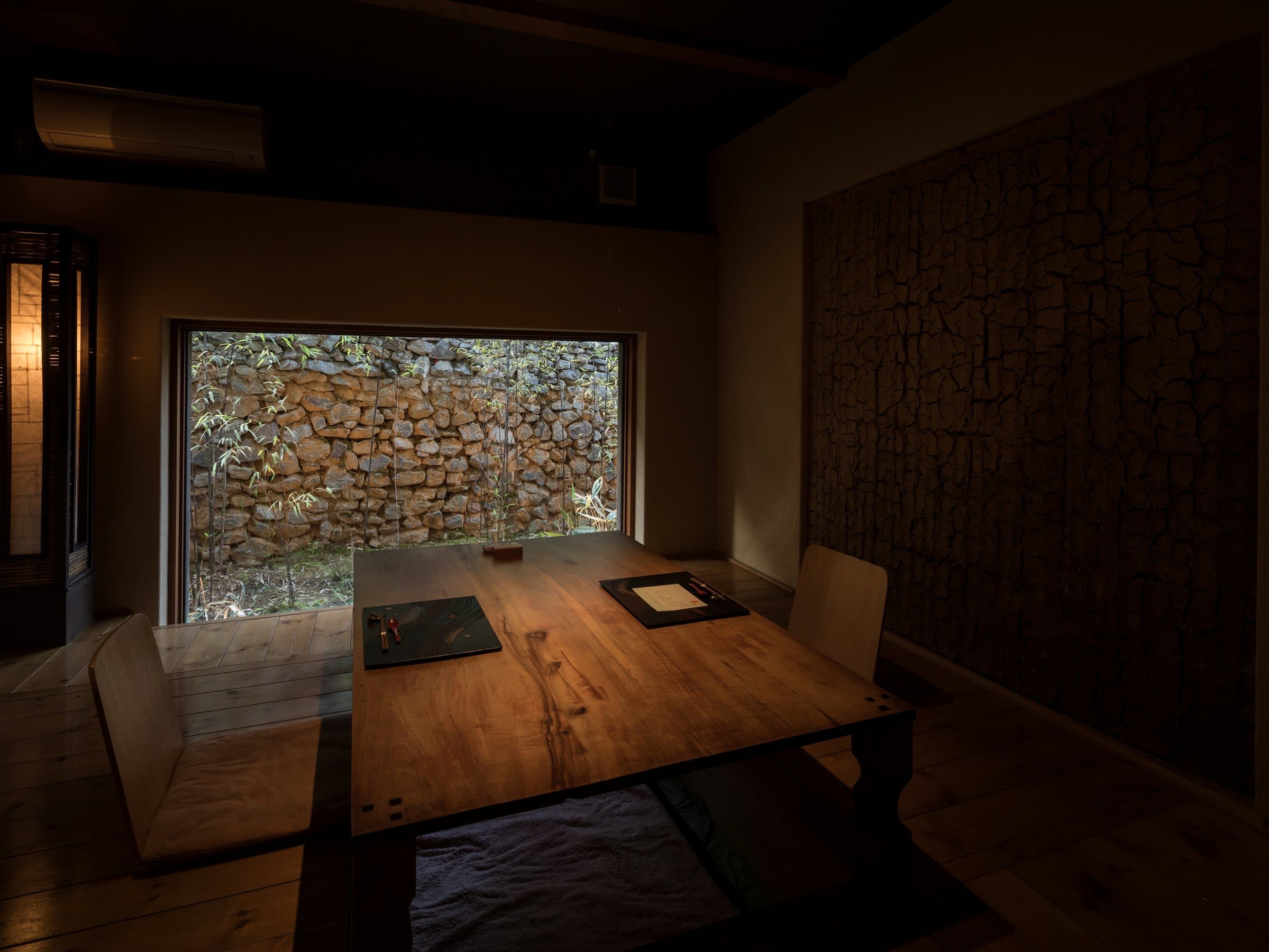 Private dining room with a wooden table and sunken kotatsu overlooking a dry stone wall garden at Ikkoten