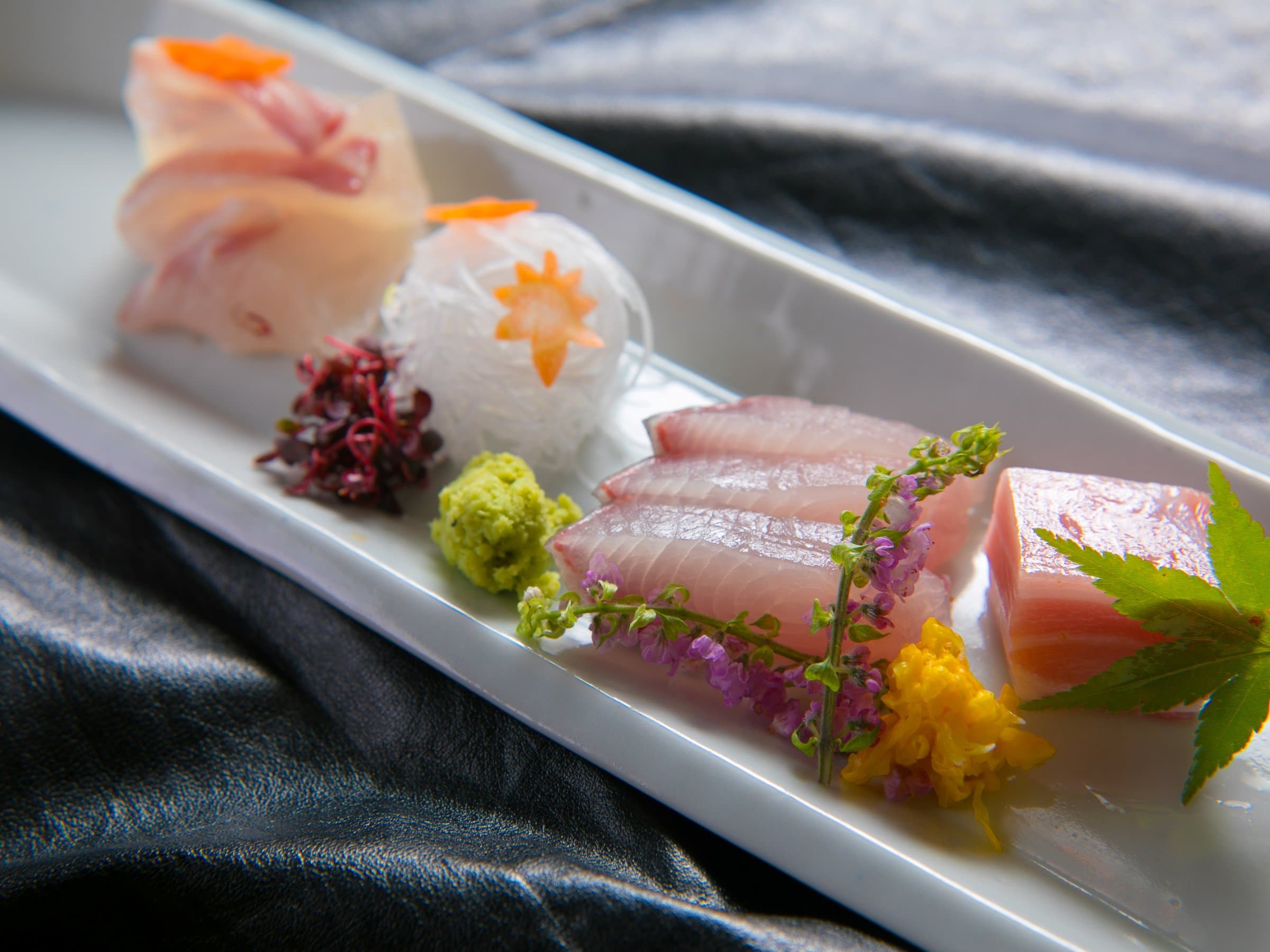 Kaiseki sashimi course of sliced fish garnished with edible flowers on a white serving plate at Ikkoten