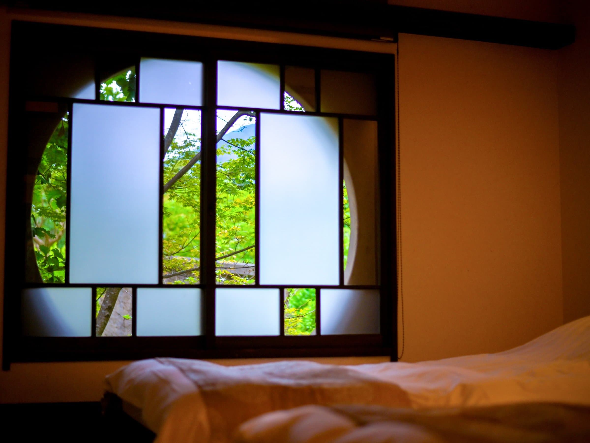 Spacious tatami guest room with low wooden table, exposed beam ceiling and round window at Ikkoten in Yufuin