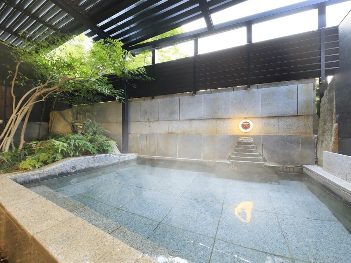 Open-air stone rotenburo bath in a private courtyard at Hotel Kikunoya on Miyajima, framed by greenery and dark stone walls