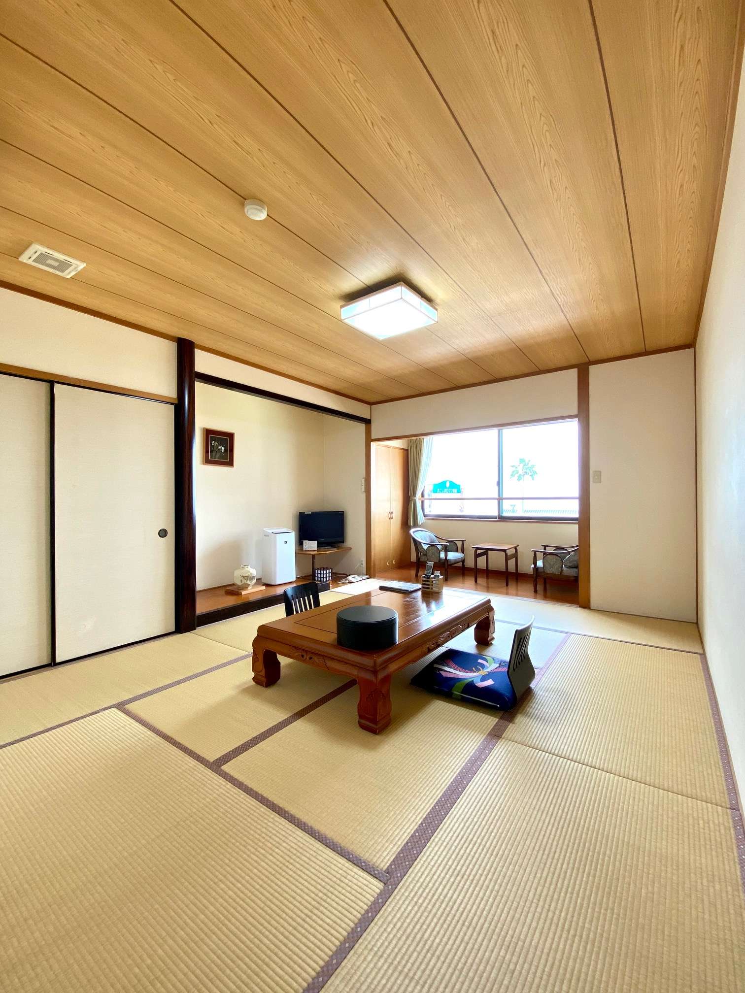 Bright wide tatami guest room with sea-view window alcove and lounge chairs at Ryokan Tsukimiso, Ibusuki Onsen