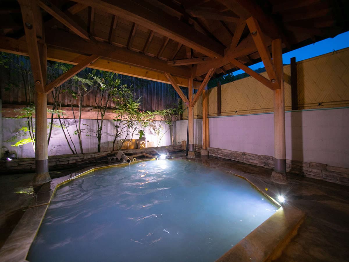 Covered open-air rotenburo hot spring bath at twilight surrounded by timber posts at Oyado Ichizen