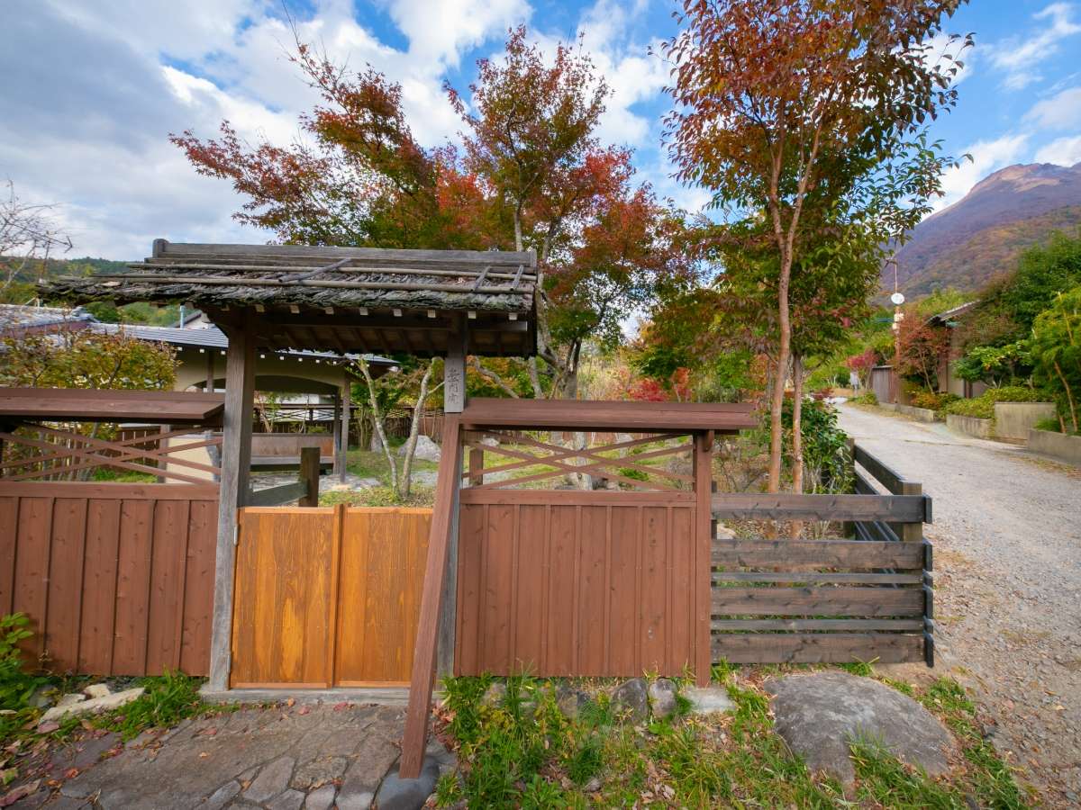Wooden entrance gate of Oyado Ichizen framed by autumn foliage and the Yufuin mountains