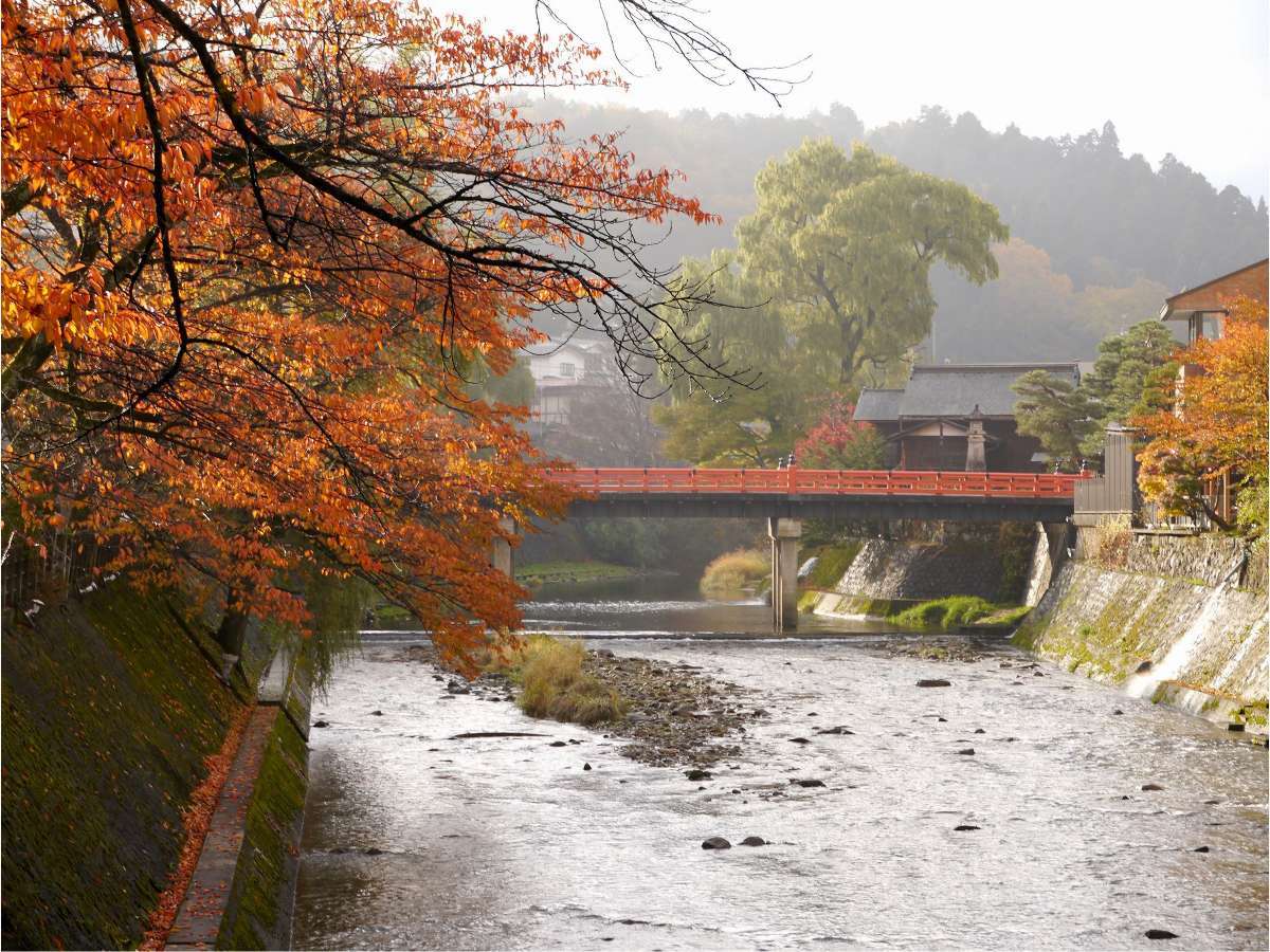 Red Nakabashi bridge over the Miyagawa river framed by autumn foliage in Takayama old town near Hodakaso Yamano Iori