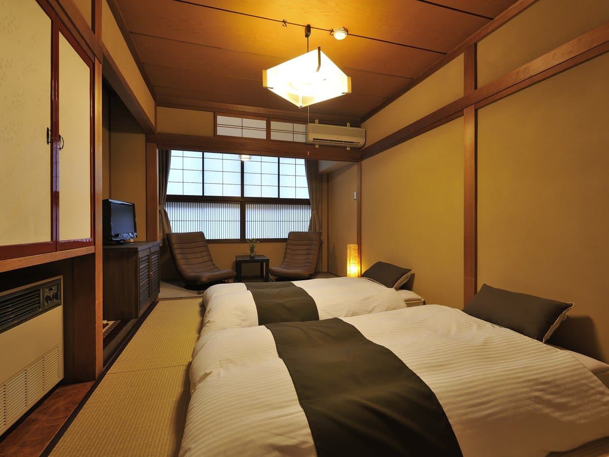 Tatami twin guest room with futon bedding, leather lounge chairs and a TV at Hida Takayama Hodakaso Yamano Iori