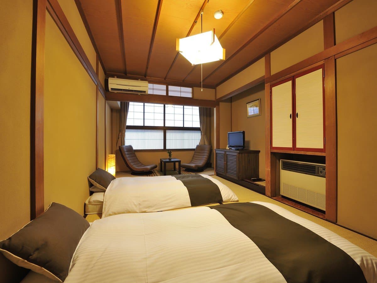 Warmly lit tatami guest room with twin futon beds, paper lantern fixture and wood-framed walls at Hodakaso Yamano Iori in Takayama