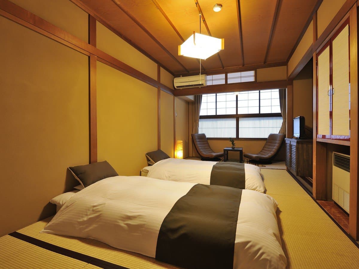 Japanese-style guest room with twin futon beds, tatami flooring, low lounge chairs and shoji windows at Hodakaso Yamano Iori