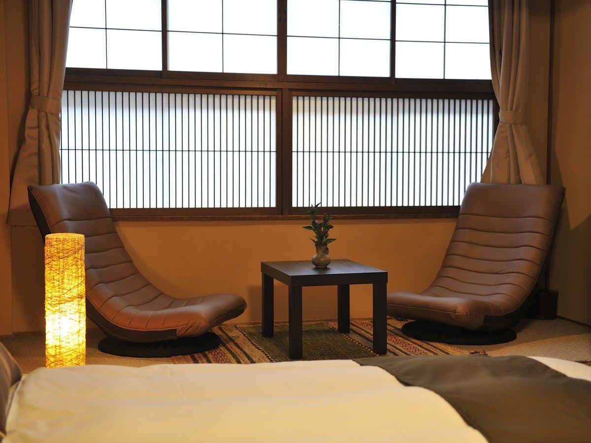 Guest room corner detail with two reclining leather chairs, low table and ikebana before latticed shoji windows at Hodakaso Yamano Iori
