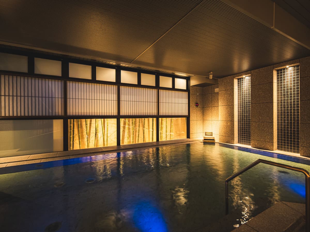 Warmly lit indoor hot-spring bath at Dogo Prince Hotel with latticed shoji panels reflecting on the water