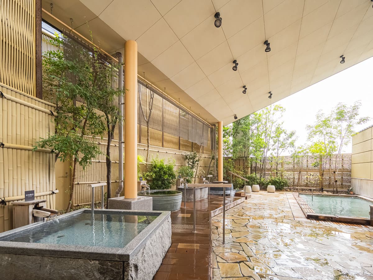 Open-air rotenburo at Dogo Prince Hotel with stone tubs, flowing spouts and a bamboo screen garden