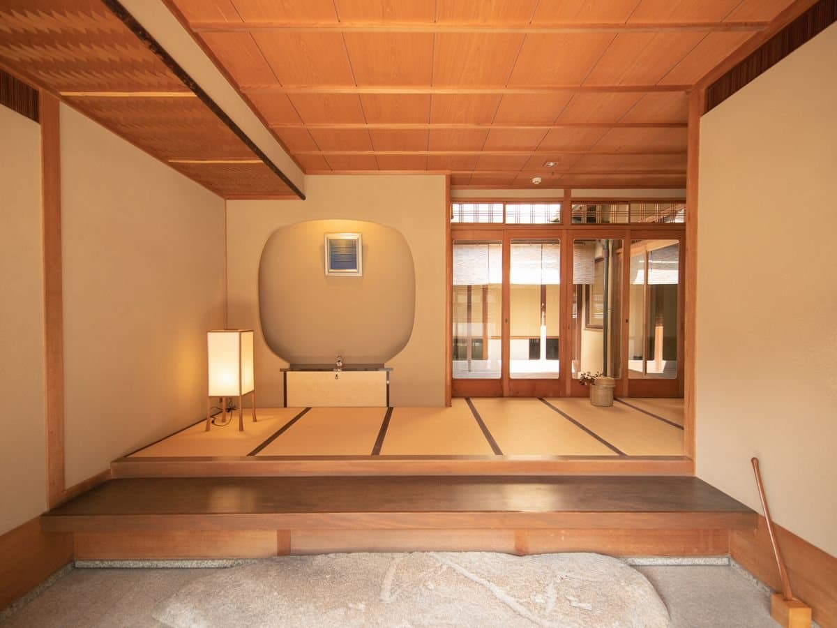 Tranquil tatami entrance hall at Umenoya with a wooden step-up, paper andon lamp and view through to an inner courtyard