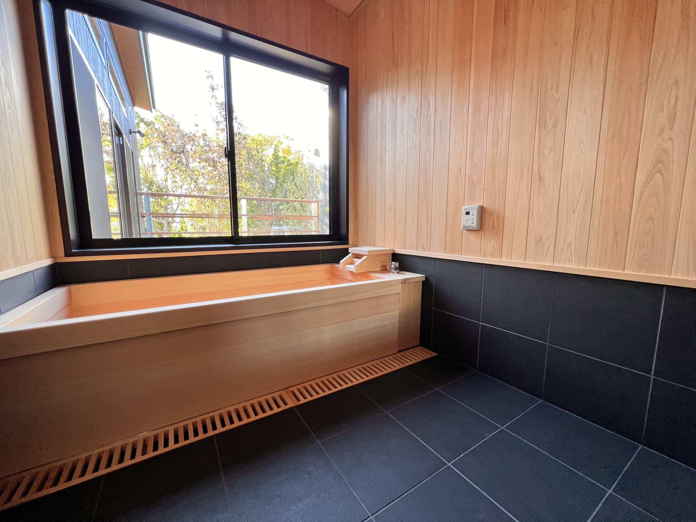 Private guest bath with hinoki cypress tub beside a large window overlooking trees at Yamanote Bettei Hagakure
